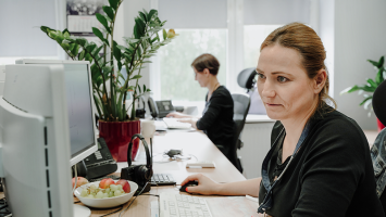 Foto einer Frau, die in einem Büro vor einem Computer sitzt und für Kundenservice zuständig ist